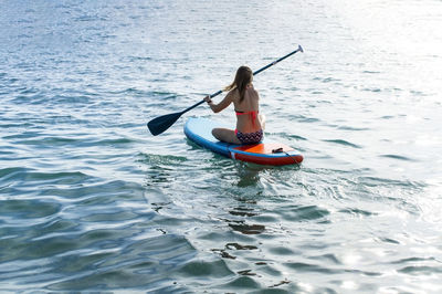 Rear view of woman paddleboarding in sea