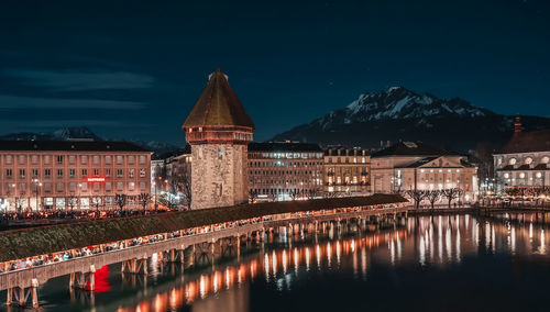 Illuminated buildings by river against sky at night