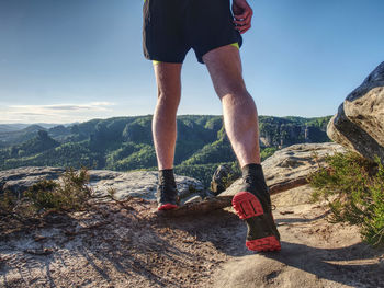 Low section of man on rock against sky