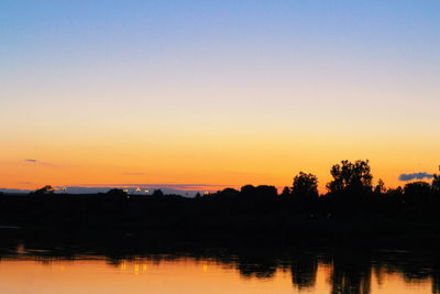 Silhouette trees by lake against romantic sky at sunset