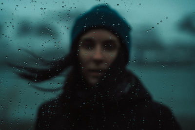 Portrait of woman standing on wet glass window