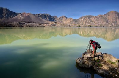 Man standing on rock by lake against sky