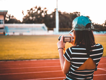 Rear view of woman photographing with camera at sports track