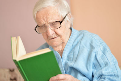 Old senior woman 90 years old holding open paper book in hands, reading best seller novel leisure