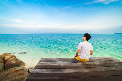 Rear view of woman sitting on sea against sky