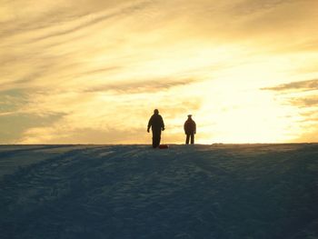 Silhouette friends walking on beach during sunset