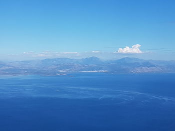 Aerial view of sea and mountains against blue sky