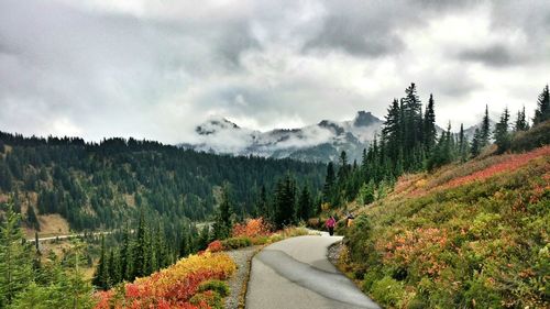 Person walking on pavement through mountains against cloudy sky