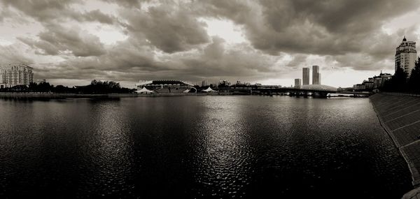 View of buildings by river against cloudy sky