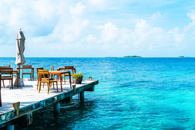 Chairs and table by sea against sky