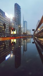 Illuminated buildings by river against sky in city