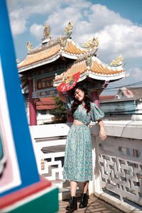 Portrait of woman in blue modern cheongsam holding a red fan at chinese temple 