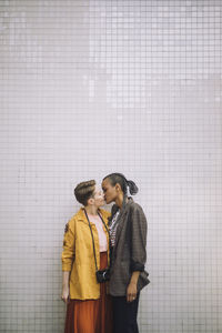 Affectionate lesbian couple kissing while standing against wall