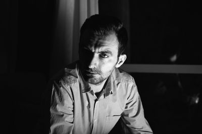 Portrait of serious young man sitting against window