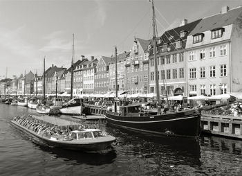 Boats moored on canal by buildings in city against sky