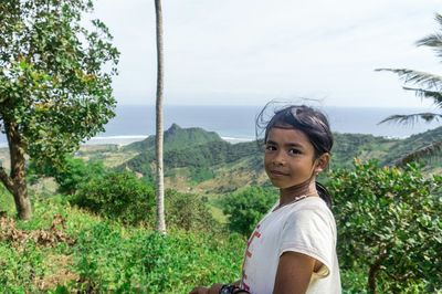 Portrait of young woman against plants and trees against sky