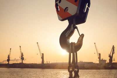 Cranes at commercial dock against sky during sunset