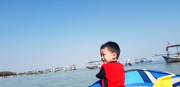Cute boy in sea against clear blue sky