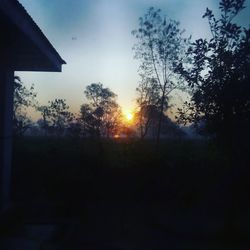 Silhouette house on field against sky at sunset