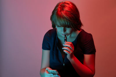 Woman using phone while smoking electronic cigarette against colored background