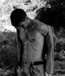 Shirtless young man standing against trees