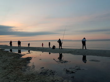 People on beach against sky during sunset