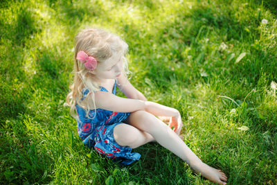 Sad young girl sitting on ground outdoor on summer sunny day. pensive little child dreaming 