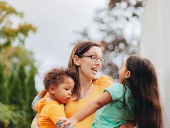 Young millennial mother at home playing with her two mixed race children in backyard