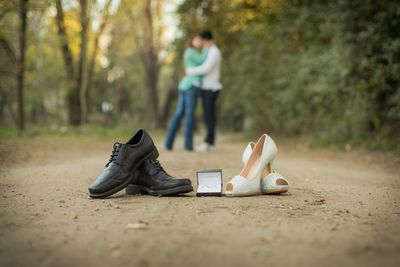 Full length of couple kissing with shoes and jewelry box in foreground at forest