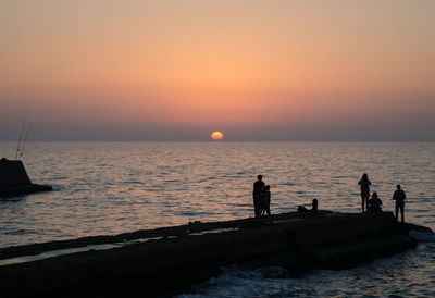 Silhouette people on pier in sea against clear sky during sunset