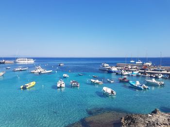 Sailboats moored in sea against clear blue sky