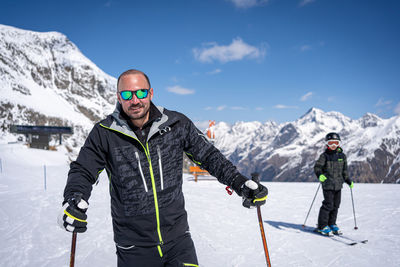 Young man with ski makes pose in mountains behind