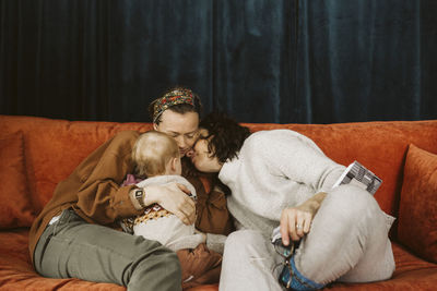 Lesbian mothers with daughter sitting on sofa at home