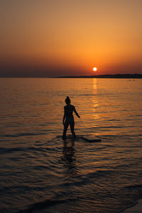 Silhouette girl wading in sea against sky during sunset