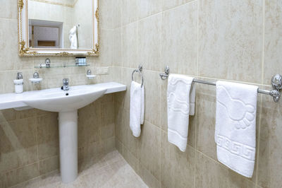 Bathroom with white sink and toilet white bathrobes for guests hang on the wall.