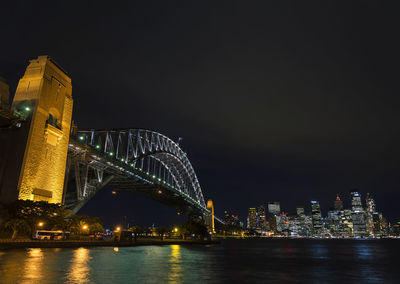 Illuminated buildings by river against sky at night