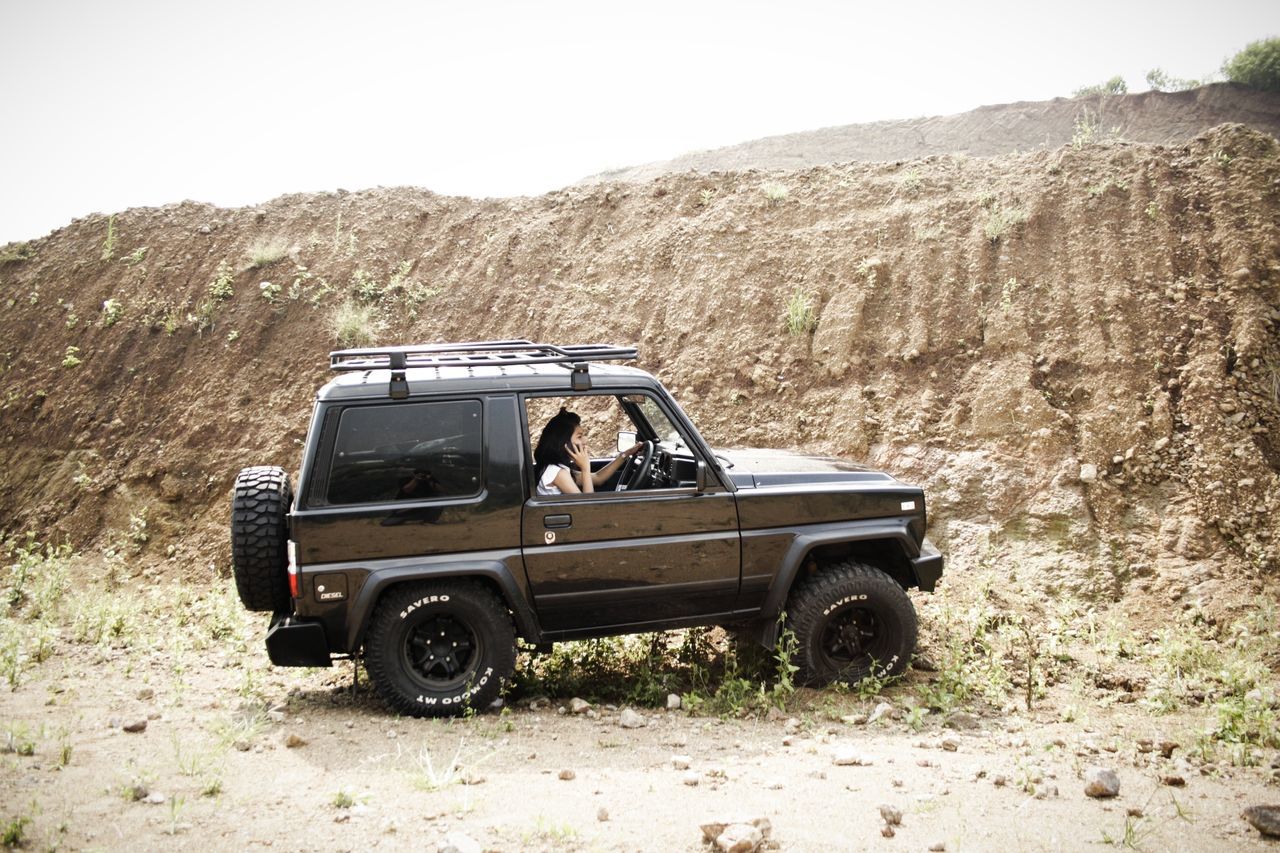 transportation, land vehicle, mode of transport, car, mountain, travel, landscape, clear sky, road, on the move, nature, day, non-urban scene, desert, outdoors, mountain range, rock - object, sky, journey, vehicle