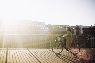 Side view of female businesswoman riding bicycle on road during sunny day