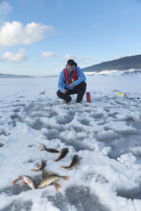 Fisherman fishing on snow covered lake against sky