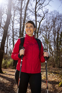 The smiling young woman is hiking in the woods. 