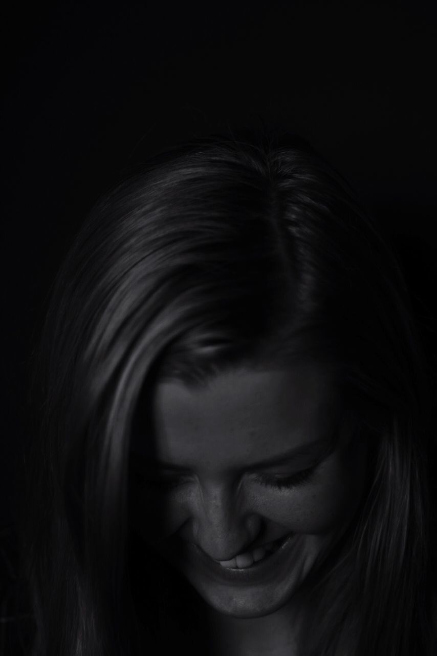 CLOSE-UP OF YOUNG WOMAN WITH HAIR OVER BLACK BACKGROUND