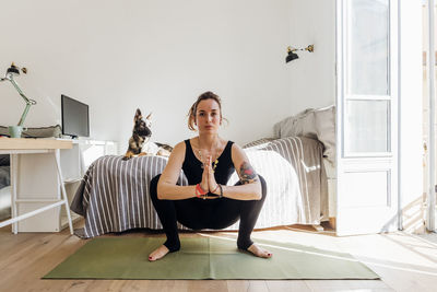 Woman with hands clasped crouching on exercise mat in bedroom