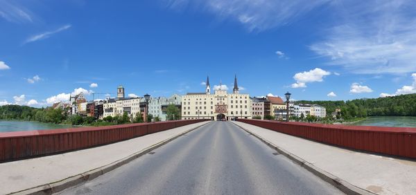 Road passing through buildings against cloudy sky