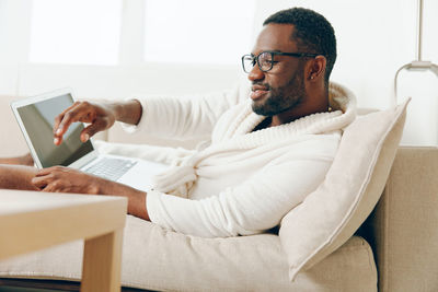 Young man using laptop while sitting on bed at home