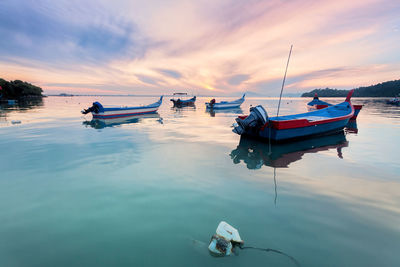 Boats moored on sea against sky during sunset