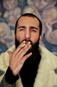 Portrait of young man smoking cigarette against wall