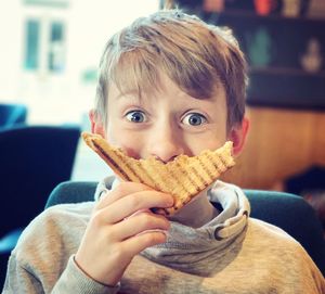 Close-up portrait of boy covering mouth with bread at home