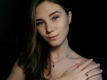 Close-up portrait of beautiful young woman wearing necklace against black background