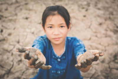 High angle portrait of girl showing dirty hands on cracked field