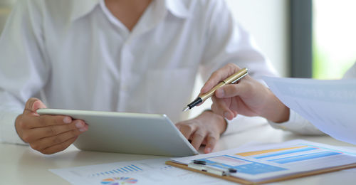 Midsection of businessman showing digital tablet to colleague